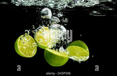 Citron vert éclaboussant avec des bulles dans l'eau isolée contre arrière-plan noir Banque D'Images