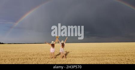 Dans un champ de blé après la pluie, deux filles courent.Un véritable arc-en-ciel coloré à l'horizon. europe Ukraine.Champs de culture d'été, mûrs Banque D'Images