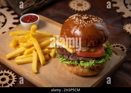 Les hamburgers de bœuf sont servis avec des frites sur un panneau décoratif en bois avec une sauce tomate et des morceaux décoratifs en bois de simple Banque D'Images