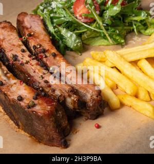 Côtelettes de rechange au barbecue servies avec des frites et une salade d'arugula avec des tomates cerises et du parmesan servis à bord recouverts de Banque D'Images