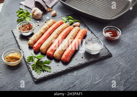 Saucisses de viande crues sur une plaque d'ardoise, avec herbes et épices et une poêle à grillades carrée.Vue de dessus Banque D'Images