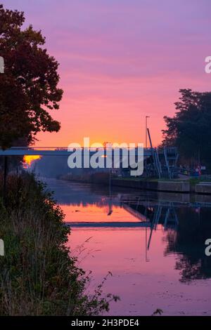 Le canal du ruisseau et un pont avec des bancs d'herbe et des fleurs sauvages et des arbres dans un paysage pittoresque sur un brumeux autumns matin soleil Banque D'Images