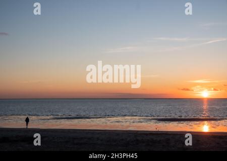 Vue sur les silhouettes des personnes marchant dans le soleil couchant sur la mer et réfléchi sur la plage, nuages avec le soleil brillant Banque D'Images