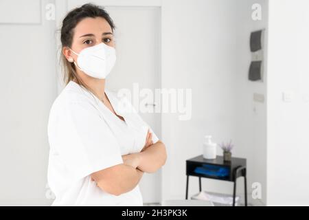 Physiothérapeute femme confiante posant dans une clinique moderne portant un masque facial protecteur pendant une pandémie de coronavirus Banque D'Images