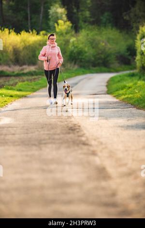 Sport fille est en train de courir avec un chien (Beagle) sur une laisse au printemps. Banque D'Images