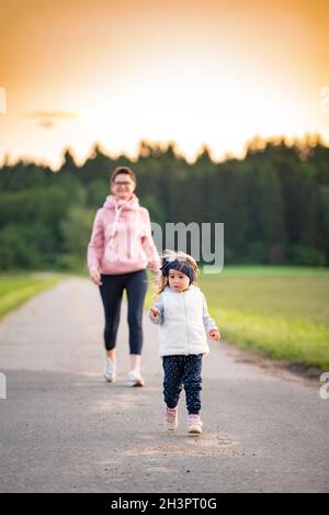 Mère et enfant marchant sur la route de campagne entre les champs agricoles vers le vilage de la forêt. Banque D'Images