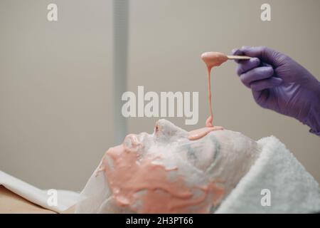 Alginate masque processus d'application. Une femelle mains d'une spatule de maintien d'esthéticienne. Femme couché sur un canapé dans le bureau de cosme Banque D'Images