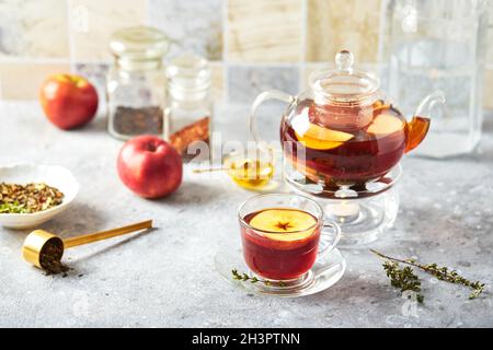 Thé aux fruits avec pommes et thym dans une théière en verre et une tasse sur la table de cuisine Banque D'Images