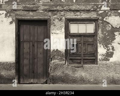 Image monochrome de l'avant d'une ancienne maison abandonnée avec fenêtres à volets et porte en bois verrouillée avec peinture écaillée Banque D'Images