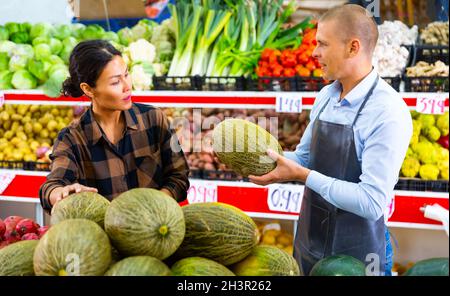 Un vendeur aidant une femelle à choisir le melon en magasin Banque D'Images