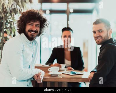 Un groupe de professionnels en pause-café utilisent des ordinateurs portables, des tablettes et des smartphones tout en discutant de nouveaux projets d'entreprise. Banque D'Images