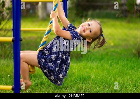 Petite fille souriante mignonne 1-3, monte la corde sur l'aire de jeux extérieure pour enfants Banque D'Images