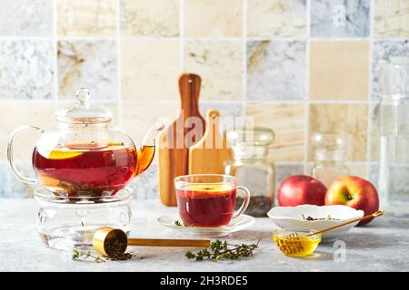 Thé aux fruits avec pommes et thym dans une théière en verre et une tasse sur la table de cuisine Banque D'Images