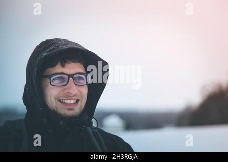 Jeune homme souriant avec capuche, à l'extérieur, en hiver Banque D'Images