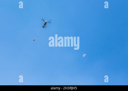 Hélicoptère allant dans la zone de feu pour éteindre le feu de forêt.hélicoptère avec un seau d'eau sur un ciel bleu.hélicoptère de lune et de feu de forêt dans le même cadre. Banque D'Images