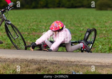 Enfant tombant de vélo, accident de rue, une fille avec un casque de vélo Banque D'Images