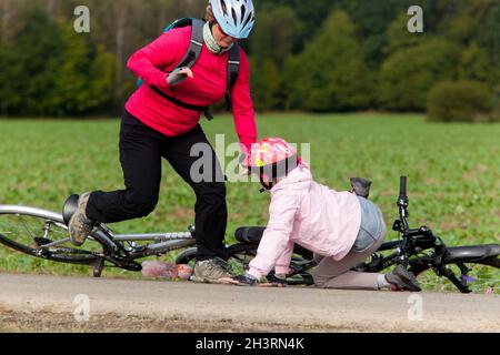 Enfant après la chute de la bicyclette, une fille avec un casque de vélo, une femme se précipitant pour l'aide Banque D'Images