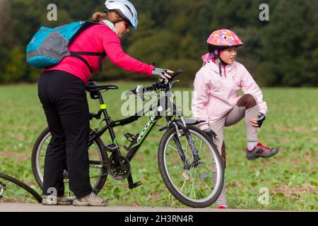 Enfant après avoir chuté du vélo, une fille avec un casque de vélo est en train de se cogner son genou Banque D'Images