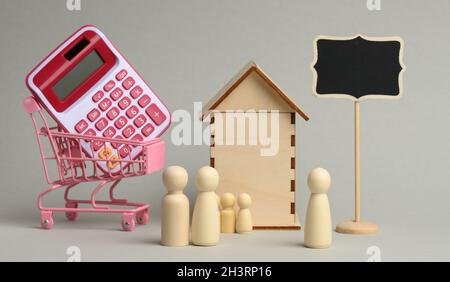 Famille de figures en bois et d'un realteur sur le fond d'une maison et d'une calculatrice dans un chariot sur un fond gris Banque D'Images