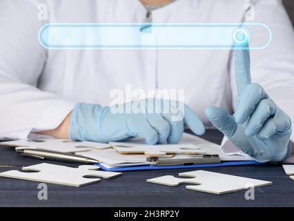 Une femme médecin est assise sur une robe blanche et des gants en latex bleu à la table Banque D'Images