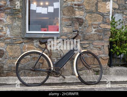 Vieux pédalier rouillé enchaîné à l'extérieur du vieux cottage rural en pierre.Vélo de poussage abandonné ayant besoin d'un peu d'huile et d'entretien avec tableau blanc de craie Banque D'Images