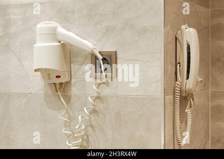 Sèche-cheveux, prise électrique et téléphone au mur de la salle de bains. Banque D'Images