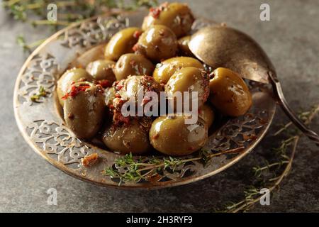 Olives vertes épicées à l'huile d'olive dans un ancien bol en métal.Bol avec olives et brindilles de thym sur une table en pierre. Banque D'Images