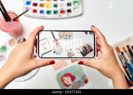 Les mains d'une femme illustratrice font une photo de son bureau avec le téléphone portable Banque D'Images