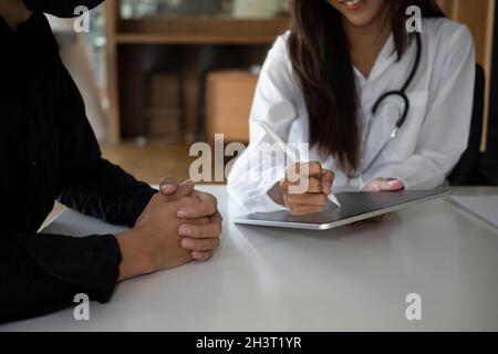 Médecin en uniforme médical blanc utilisant une tablette numérique et discutant des résultats de la vérification avec sa patiente. Banque D'Images