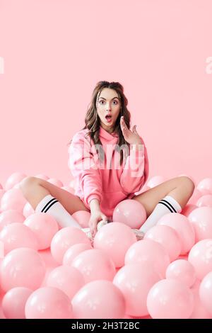 Jeune femme à la mode surprise avec des ballons roses sur fond rose pastel Banque D'Images