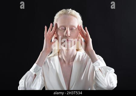 Jeune femme blonde albino faisant la gymnastique faciale automassage et des exercices rajeunissants sur fond noir Banque D'Images