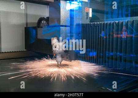 Des étincelles survolent la tête de la machine pour le traitement du métal laser en arrière-plan de l'usine métallurgique.Fabrication de pièces finies pour Banque D'Images