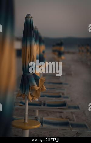 Plage au coucher du soleil avec un parasol fermé et des chaises de plage pliées. Banque D'Images