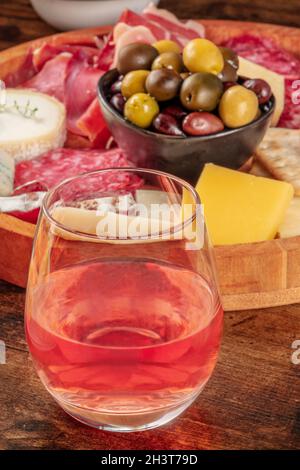 Un verre de vin de rose, en gros plan devant une planche à fromage avec des olives Banque D'Images