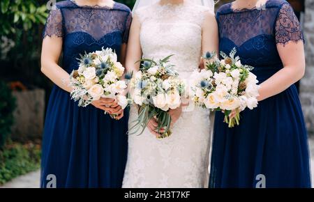 Les épouses et les demoiselles d'honneur en robes bleues identiques sont debout côte à côte et tiennent des bouquets dans leurs mains, en gros plan Banque D'Images
