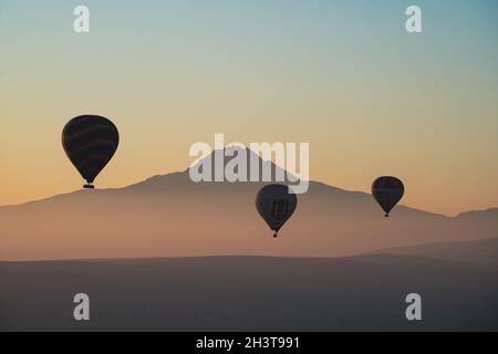 GÖREME, TURQUIE - 3 AOÛT 2021 : ballons d'air chaud colorés volant au-dessus de la vallée de la Cappadoce dans la lumière du matin avec le beau mont Erciyes pic co Banque D'Images