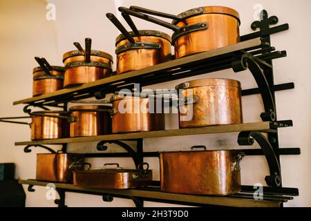 Pots, louches, plateau et casserole en cuivre, de différentes tailles, sur des étagères métalliques massives, fixées à un mur blanc. Banque D'Images