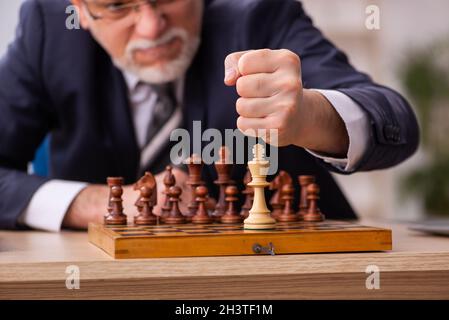 Un vieil employé de sexe masculin joue aux échecs sur le lieu de travail Banque D'Images