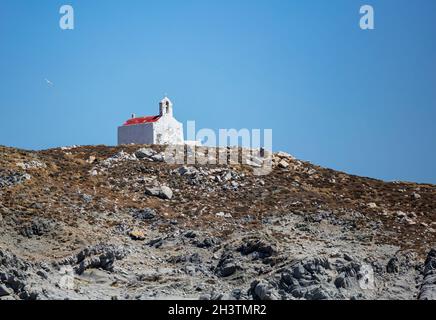 Petite ancienne chapelle, murs blancs et beffroi, toit rouge.Église grecque orthodoxe sur la colline rocheuse, ciel bleu clair.Île de Mykonos, Grèce Banque D'Images
