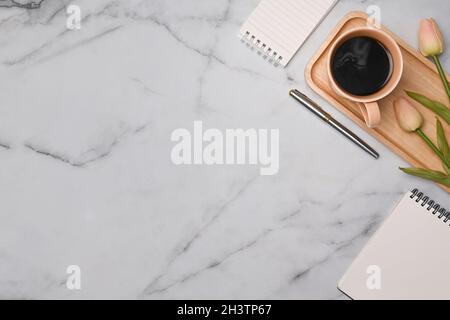 Vue de dessus tasse de café, bloc-notes et tulipes roses sur table en marbre. Banque D'Images