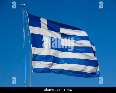 Le drapeau national de la Grèce sur le mât se développe dans le vent contre le ciel bleu Banque D'Images