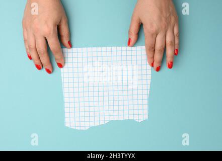 Main féminine tenant une feuille de papier vierge déchirée dans une cage sur fond bleu Banque D'Images