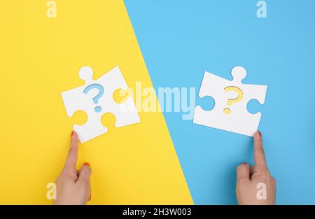 Main femelle tient un fragment d'un grand puzzle blanc sur fond bleu jaune, concept de trouver une idée Banque D'Images