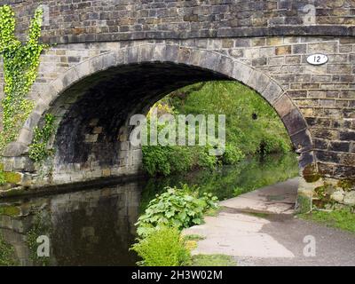 Un vieux pont en pierre traversant le canal de rochdale à mytholmroyd West yorkshire avec un sentier au bord de l'eau entouré d'arbres et b Banque D'Images