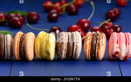 Macarons multicolores et cerises rouges mûres sur fond de bois bleu Banque D'Images