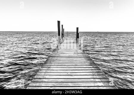 Une vue en noir et blanc d'un quai en bois qui mène dans un océan calme Banque D'Images