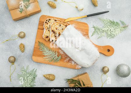 Composition de Noël avec gâteau traditionnel de stollen sur une planche en bois, couverts et cadeau sur table grise Banque D'Images