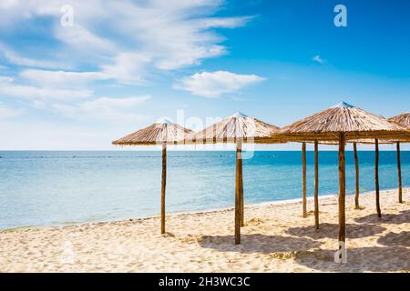 Rangée de parasols en bois à la plage de sable, mer et ciel bleu Banque D'Images