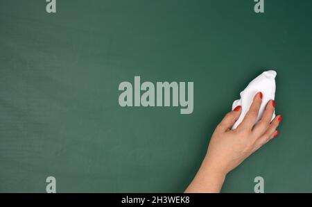La main d'une femme tient un chiffon blanc sur le fond d'un tableau de craie vert Banque D'Images