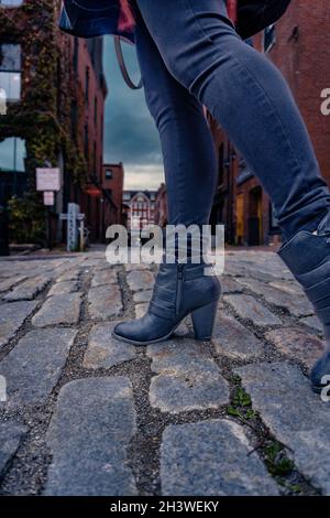 Une femme portant un Jean et des bottes noires descend dans une rue pavée. Banque D'Images